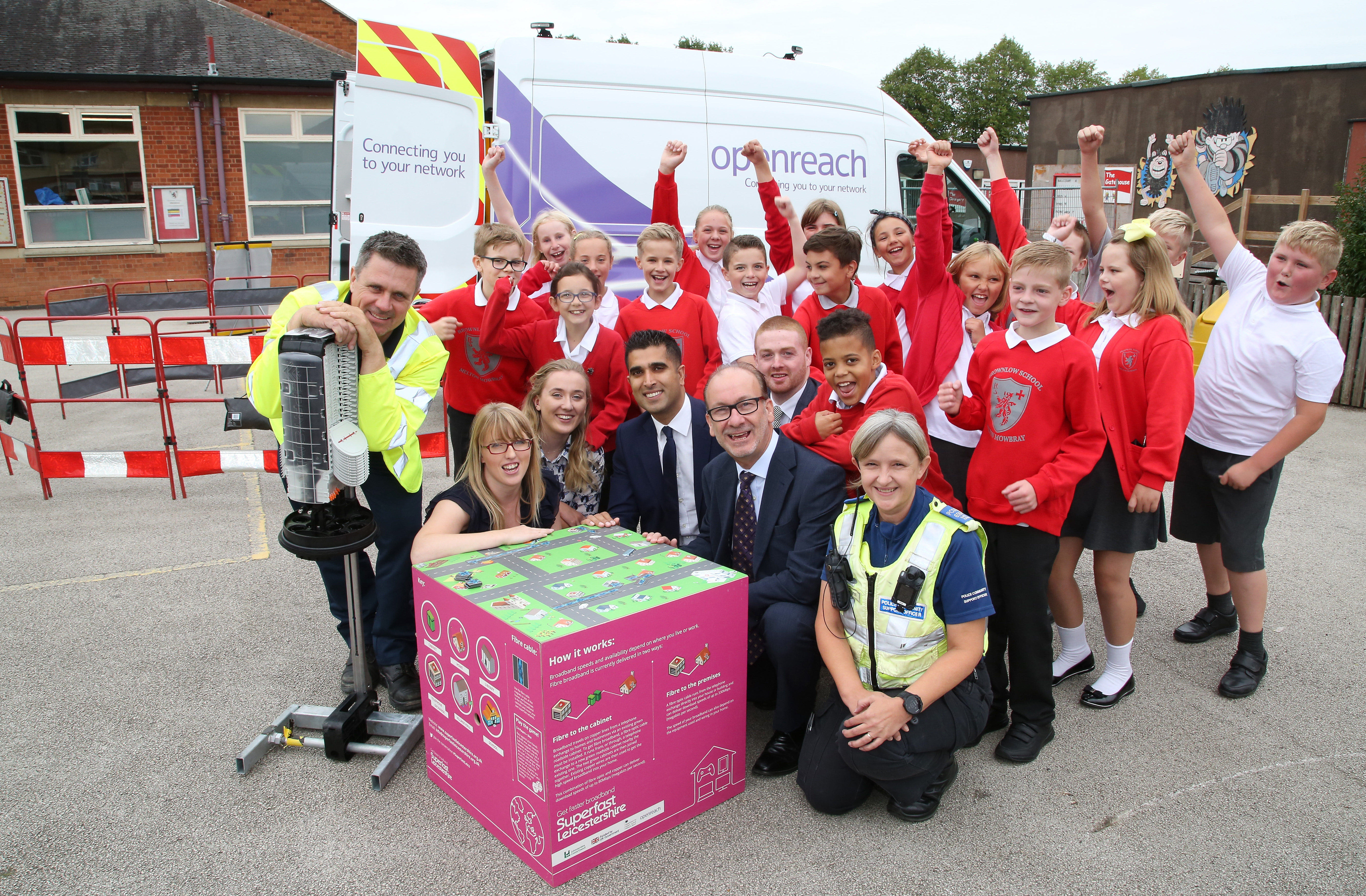 Brownlow Primary School children with representatives from Openreach, BT, Leicestershire Police and Leicestershire County Council all stood around broadband cube board game with Openreach van in background
