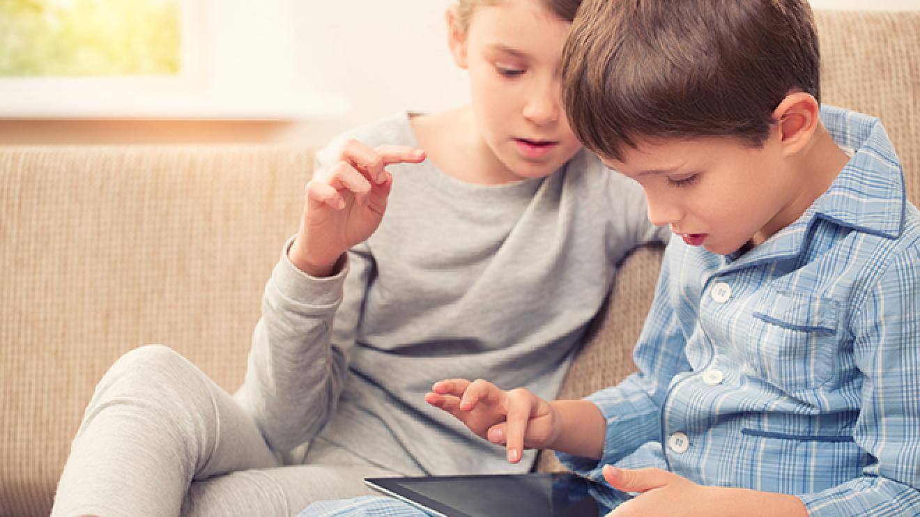 Two young boys sat on a sofa using a tablet